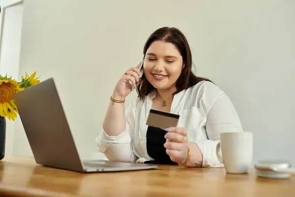 Женщина plus size улыбается, делая покупки в Интернете и потягивая кофе в своем уютном доме. — стоковое фото