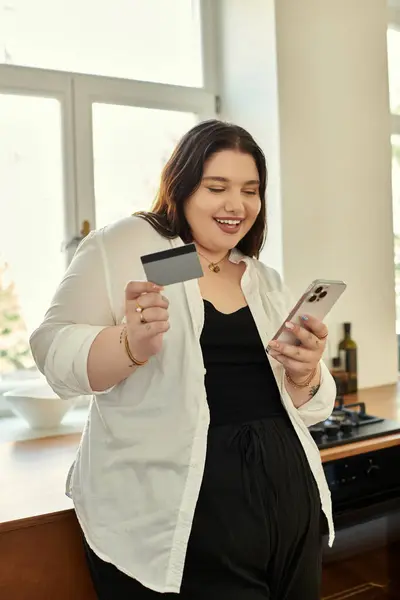 Smiling plus size woman enjoys online shopping while holding a credit card. — Stock Photo