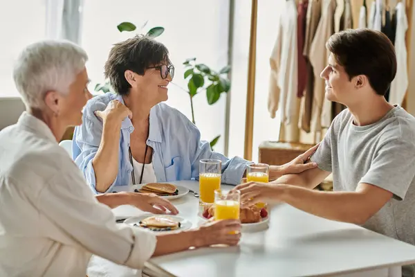 Lesbian parents and their adult son share a joyful breakfast at a sunlit table, filled with love and laughter. — Stock Photo