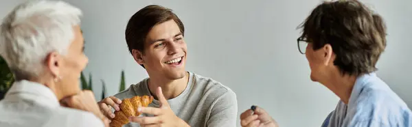 Une matinée chaude comme un couple de lesbiennes et leur fils adulte partagent sourires et petit déjeuner dans leur maison. — Photo de stock