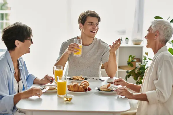 A joyful morning as a lesbian couple and their adult son share breakfast and laughter at the table. — Stock Photo
