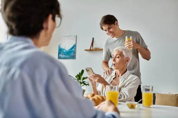 A loving LGBTQ family enjoys breakfast together, sharing laughter and technology in their sunlit kitchen. — Stock Photo
