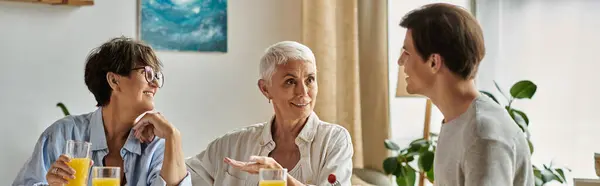 Lesbian parents enjoy breakfast together, sharing laughter and stories with their adult son in a cozy setting. — Stock Photo