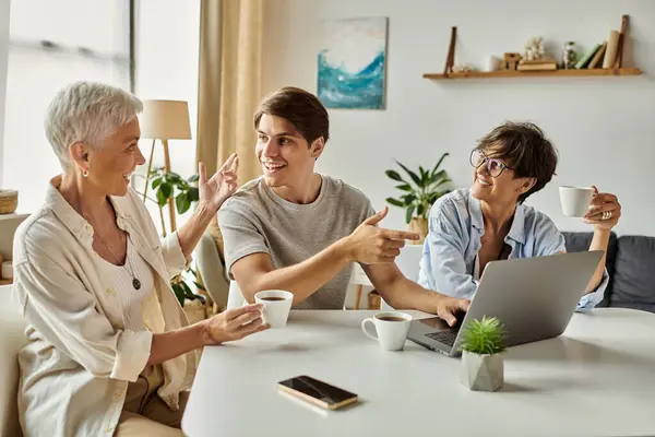 Two loving moms share a joyful moment with their adult son over coffee and laughter in a cozy home. — Stock Photo