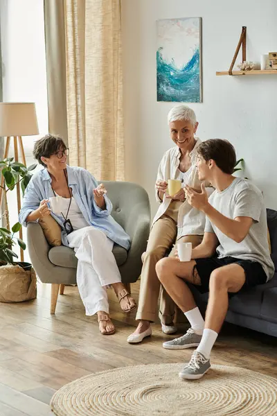 Lesbian parents and their adult son share laughter and stories in a cozy living room setting. — Stock Photo