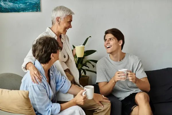 A joyful LGBTQ family shares laughter and warm drinks while relaxing in their cozy living room. — Stock Photo