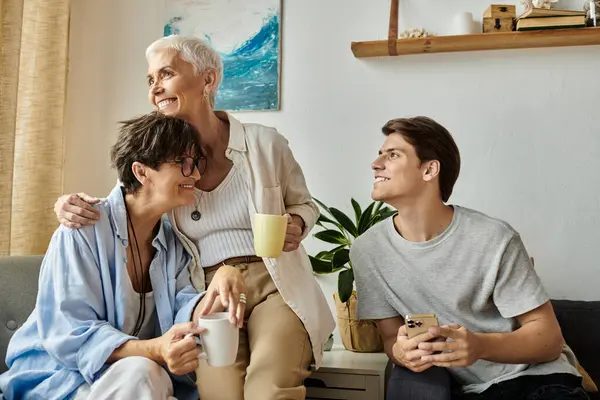 A loving LGBTQ family shares laughter and warm drinks in a cozy living room filled with joy. — Stock Photo