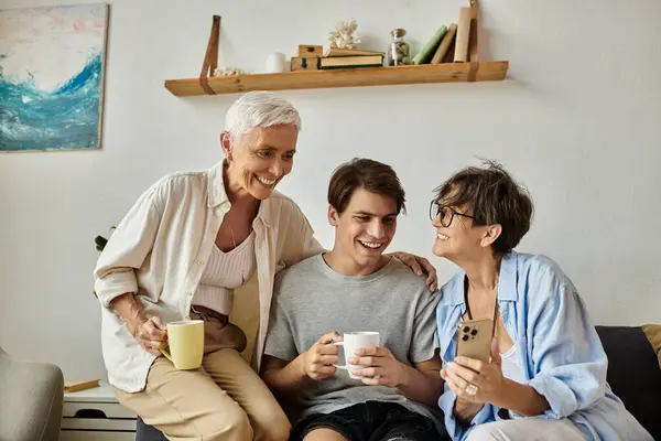 Dos madres cariñosas y su hijo adulto comparten la risa y el calor en un acogedor espacio de vida. - foto de stock