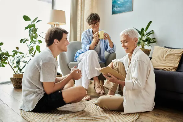 Lesbian parents and their adult son share a joyful afternoon, enjoying tea and reading together. — Stock Photo