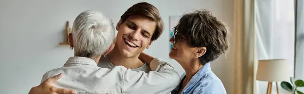 A warm family embrace unfolds as two mothers share joyful moments with their adult son. — Stock Photo