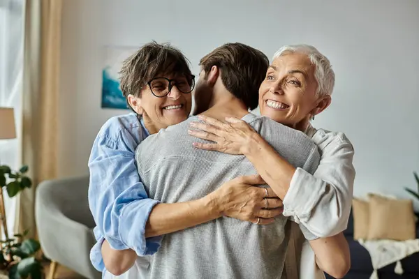 Lesbian parents and their adult son share warm hugs and laughter in their cozy living room. — Stock Photo