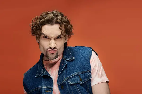 A man with curly hair poses emotionally on a striking orange background. — Stock Photo