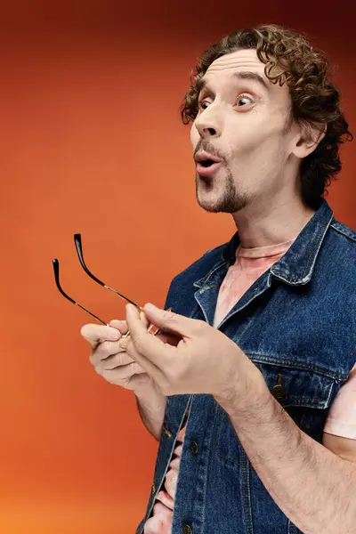 A surprised man with curly hair joyfully holds sunglasses, showcasing lively emotions. — Stock Photo