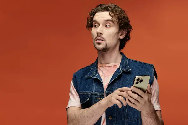 A handsome man displays emotions while holding a smartphone. — Stock Photo