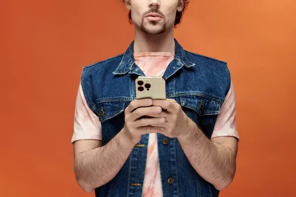 Handsome man expresses emotions while holding a smartphone before a vivid backdrop. — Stock Photo