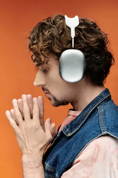 Un bell'uomo posa pensieroso, mani piegate, con le cuffie su uno sfondo arancione vivace. — Foto stock