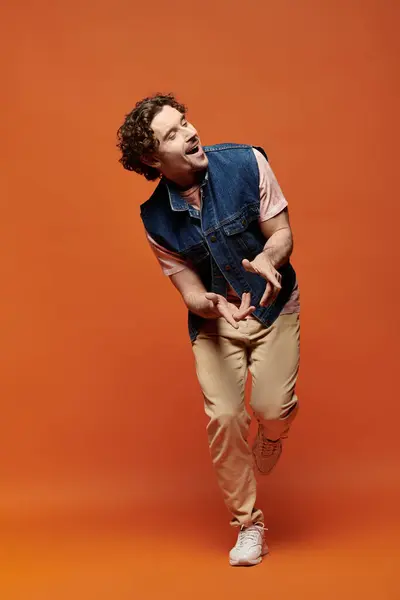 An expressive man joyfully poses in front of a bright orange background. — Stock Photo