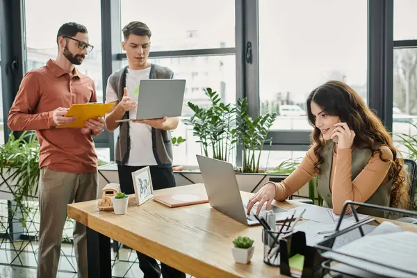 Dos colegas conversan mientras uno trabaja en un escritorio en la oficina. — Stock Photo