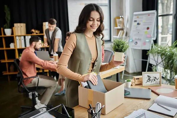 Woman organize belongings amidst a challenging layoff process, colleagues on backdrop. — Stock Photo