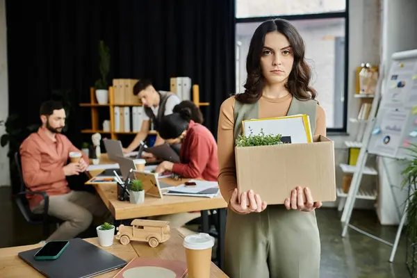 Mujer expresar emociones mixtas mientras navega por una situación de despido desafiante, colegas en el telón de fondo. — Stock Photo