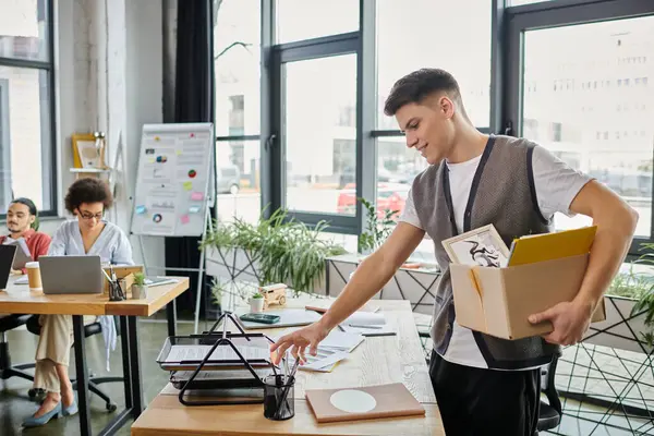 Young elegant man packing his items during lay off, colleagues on backdrop. — Stock Photo