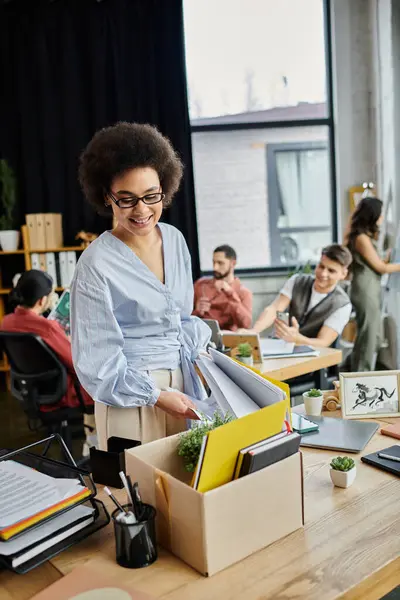 Professional african american woman packing her items during lay off, colleagues on backdrop. — Stock Photo