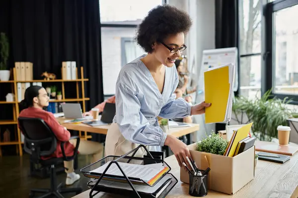 Feliz mujer afroamericana empacando sus artículos durante el despido, colegas en el fondo. - foto de stock