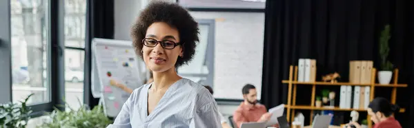 Linda mulher afro-americana embalando seus itens durante a demissão, colegas em pano de fundo. — Fotografia de Stock
