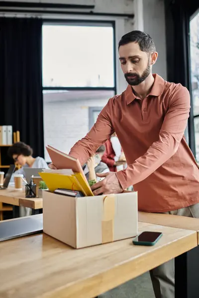 Fashionable man packing his items during lay off, colleagues on backdrop. — Stock Photo