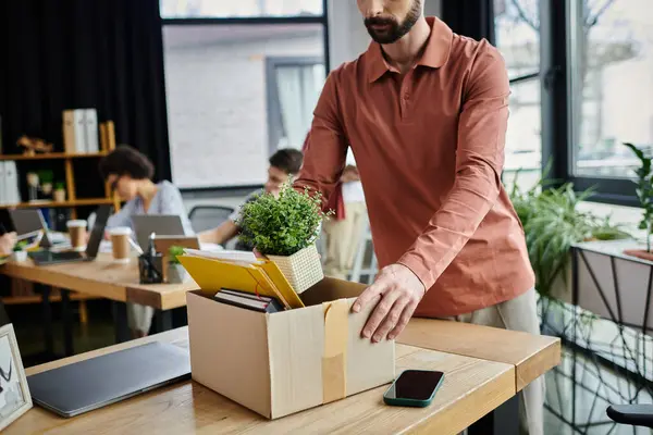 Dapper hombre embalaje de sus artículos durante el despido, colegas en el telón de fondo. — Stock Photo