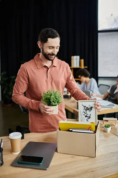 Debonair Mann packt seine Habseligkeiten während der Entlassung in modernem Büro, Kollegen im Hintergrund. — Stockfoto
