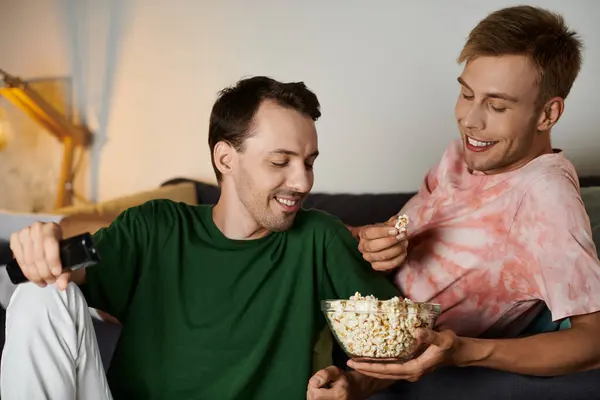 Two men share a joyful moment with popcorn while watching a movie at home. — Stock Photo