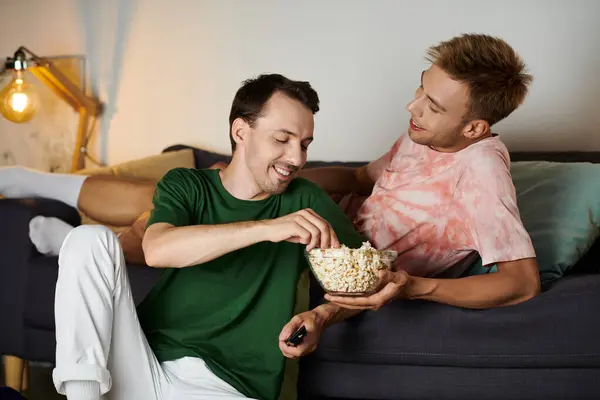 Una alegre pareja disfruta de palomitas de maíz mientras se relaja en su sofá. - foto de stock