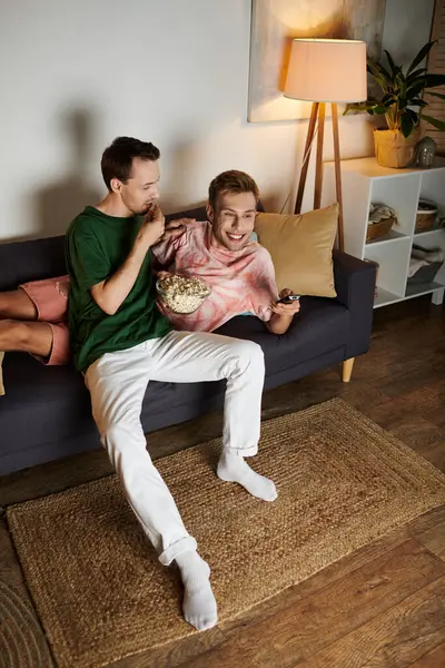 Two men sharing popcorn and laughter while relaxing on a couch. — Stock Photo