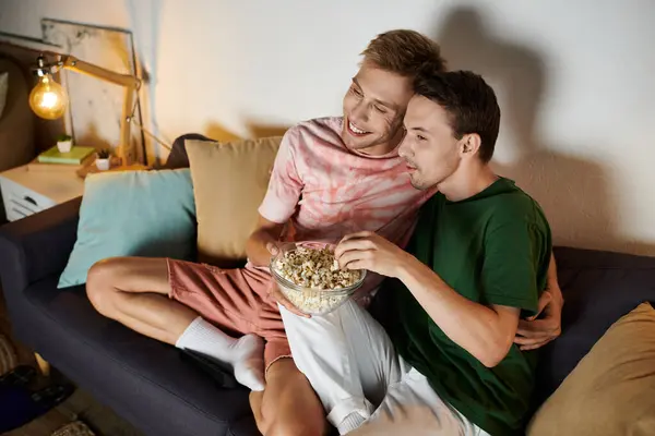 Two men snuggle on the couch, sharing laughter and popcorn during movie night. — Stock Photo