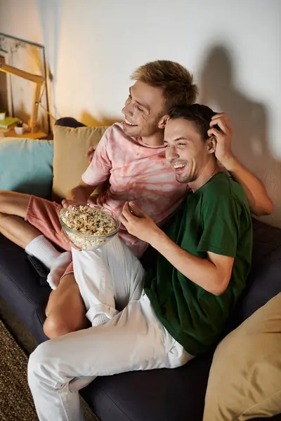 Two men share laughter and popcorn while relaxing together at home. — Stock Photo