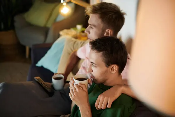 Two men share a sweet moment on the couch while sipping coffee and relaxing. — Stock Photo