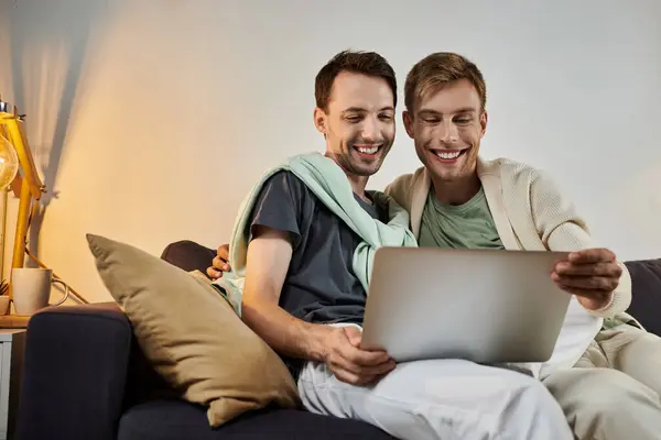 Deux hommes partagent le rire et la chaleur tout en explorant un ordinateur portable dans leur salon. — Photo de stock