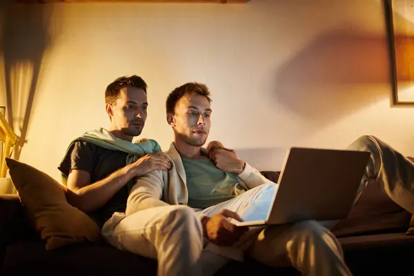 A couple shares a warm moment cuddled up on the couch, focused on their laptop. — Stock Photo