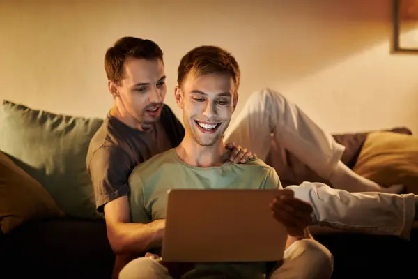 Two men enjoy time together, sharing smiles and a laptop at home. — Stock Photo