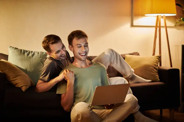 Dos hombres comparten la risa y el calor mientras se relajan juntos en el sofá. - foto de stock