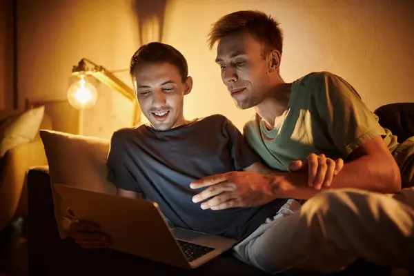 Two men share laughter and joy while using a laptop at home. — Stock Photo