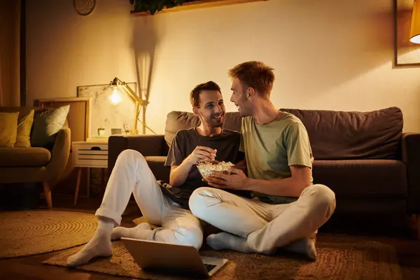 Two men enjoy quality time on the floor, sharing popcorn and smiles in their living room. — Stock Photo