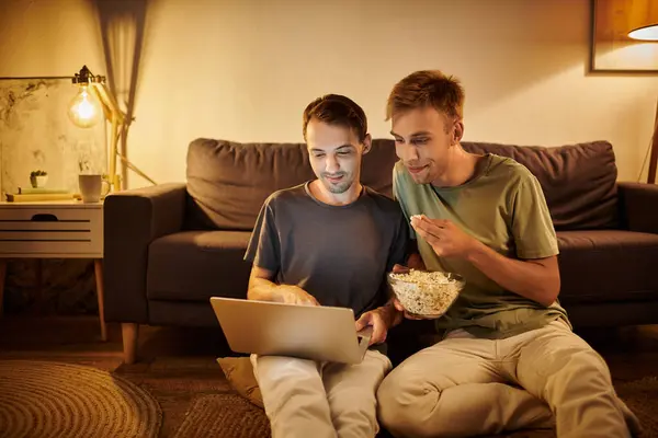 Due uomini condividono risate e snack mentre guardano un film a casa. — Foto stock