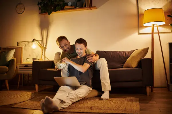 Two men share a warm moment, watching a movie and sharing popcorn at home. — Stock Photo