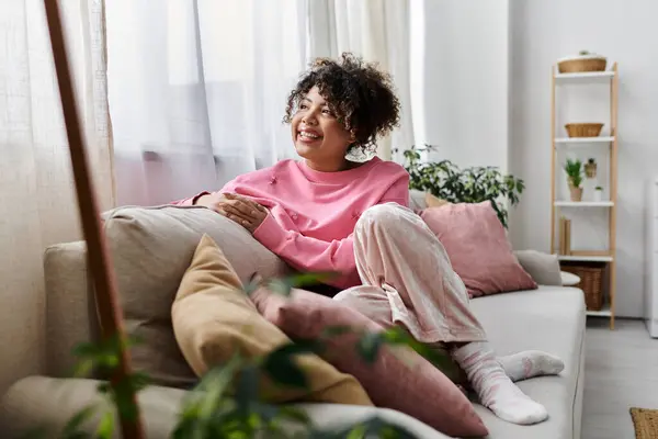 Une jeune femme joyeuse se détend confortablement à la maison, se prélassant à la lumière naturelle. — Photo de stock