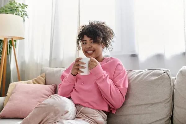 Smiling young woman relaxes on the couch, sipping coffee in a warm, inviting atmosphere. — Stock Photo