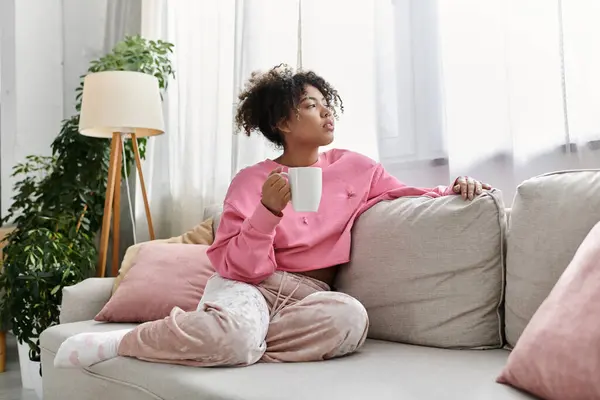 Young woman enjoys a warm drink while reflecting in her cozy living space. — Stock Photo