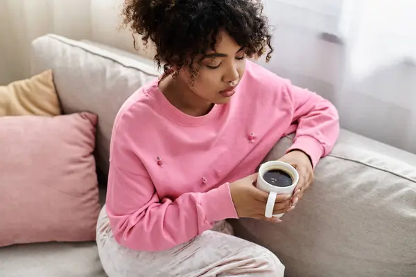 A young woman sips coffee while relaxing on the couch in her stylish living room. — Stock Photo