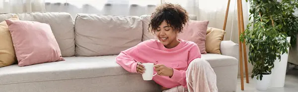 A young woman relaxes at home, sipping a warm drink and smiling contently. — Stock Photo